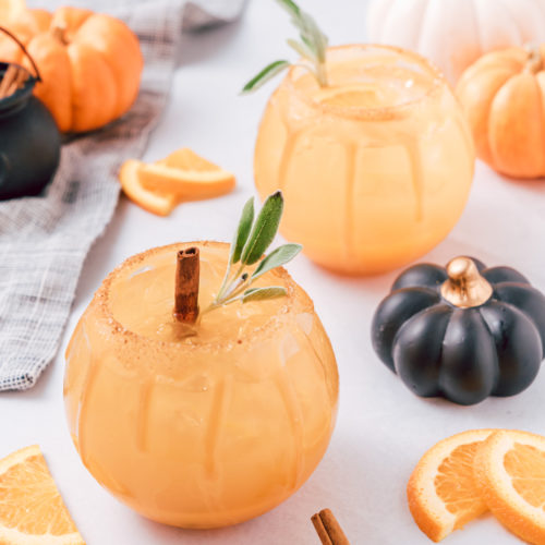 2 glasses of pumpkin punch, surrounded by pumpkins.