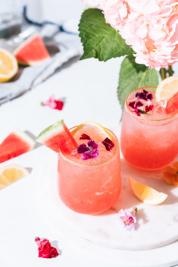 2 watermelon rose fresca cocktails on tray. Garnished with watermelon, flowers and lemon.
