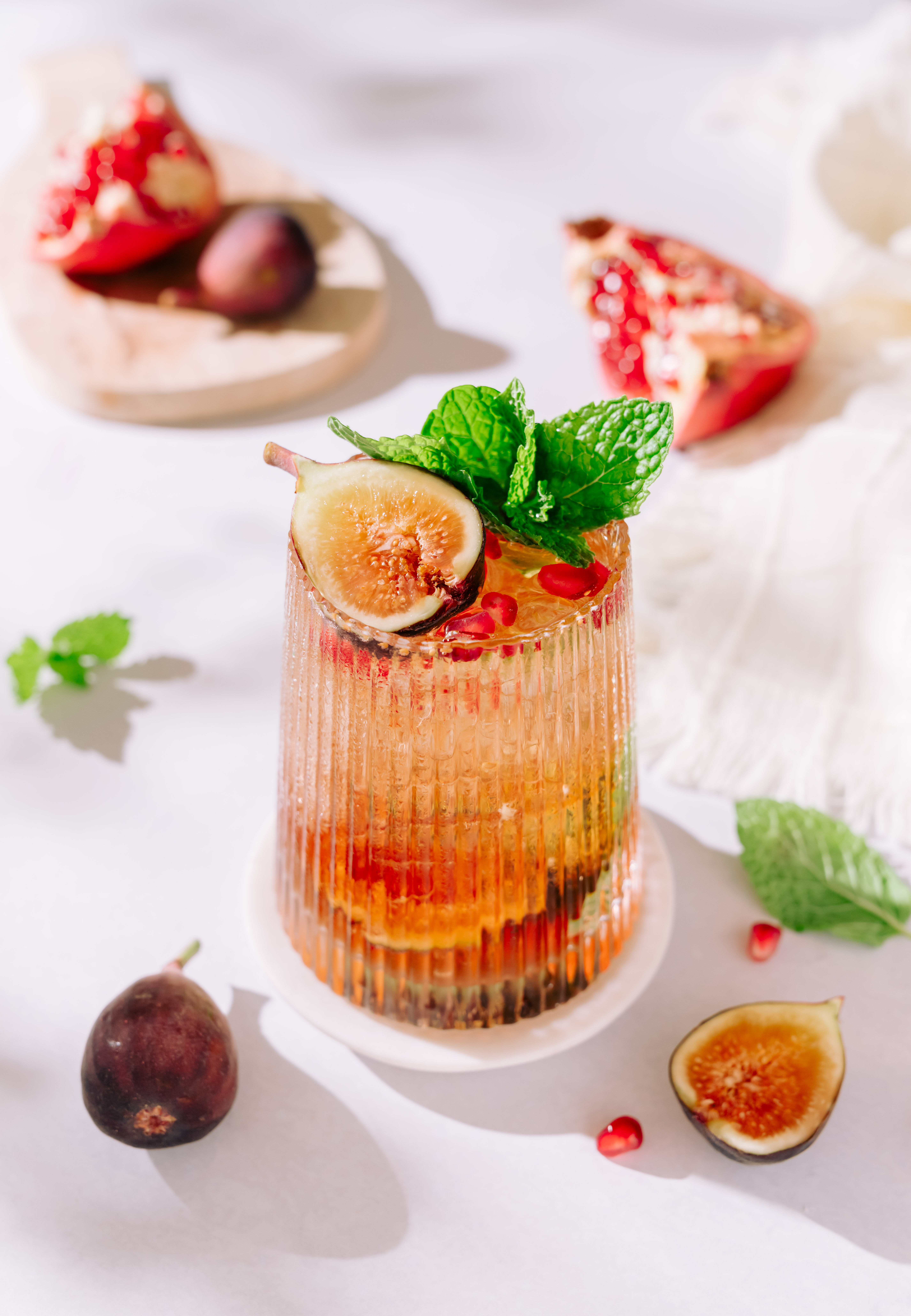 A cocktail glass is filled with reddish liquid, topped with figs, mint, and pomegranate arils.