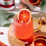 Blood Orange hot toddy in a clear mug with a slice of blood orange and cloves as garnish.