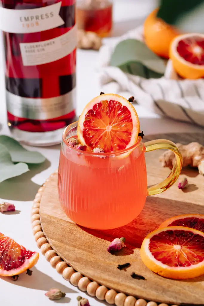 Blood Orange hot toddy in a clear mug with a slice of blood orange and cloves as garnish. 
