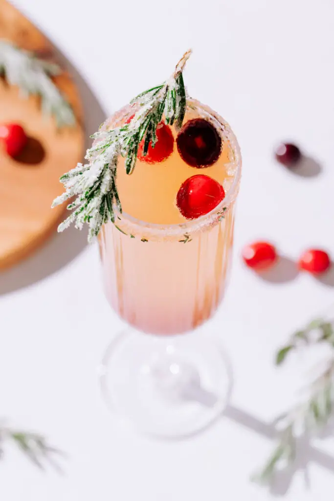 A cranberry mimosa garnished with cranberries and sugared rosemary