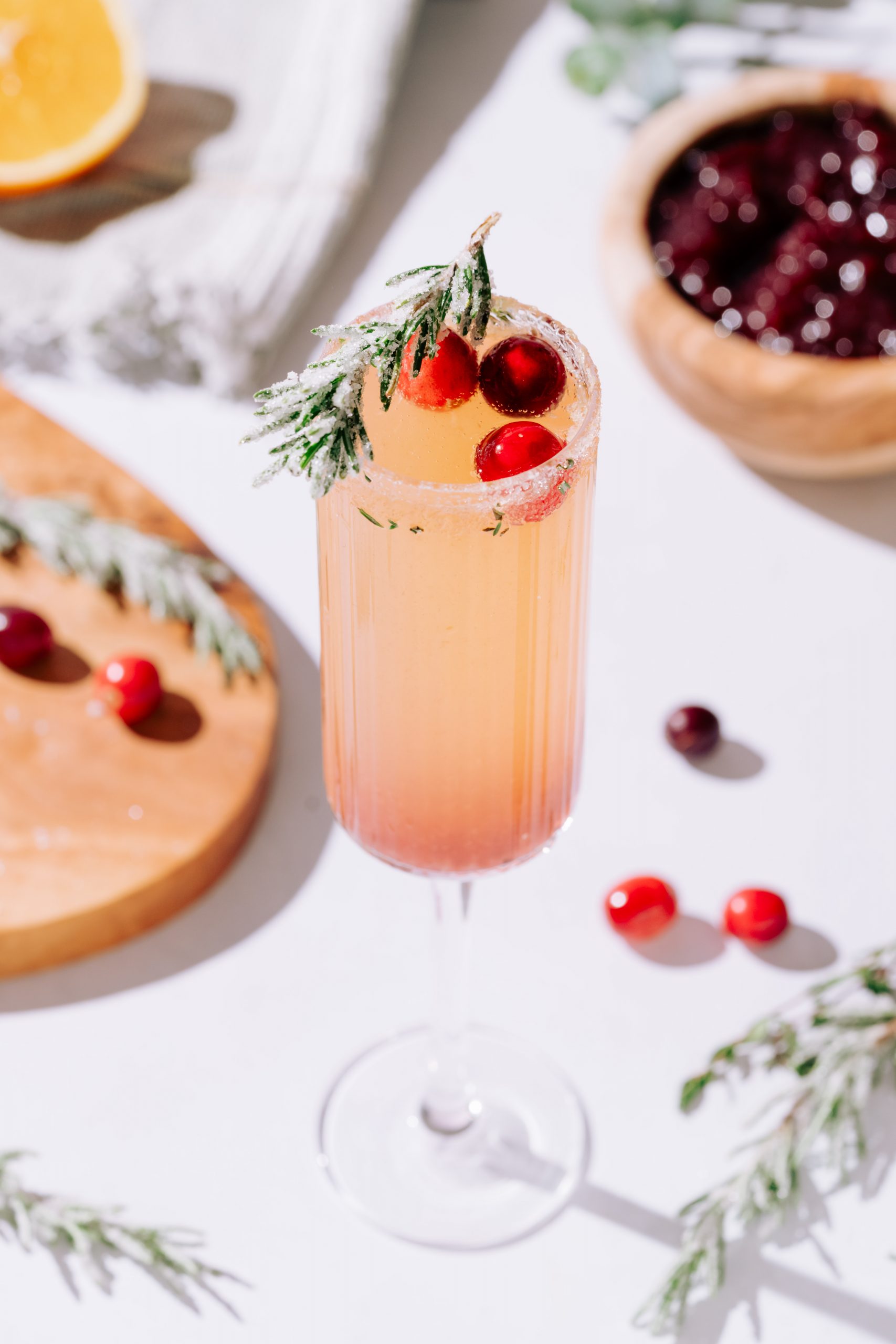A cranberry mimosa garnished with cranberries and sugared rosemary