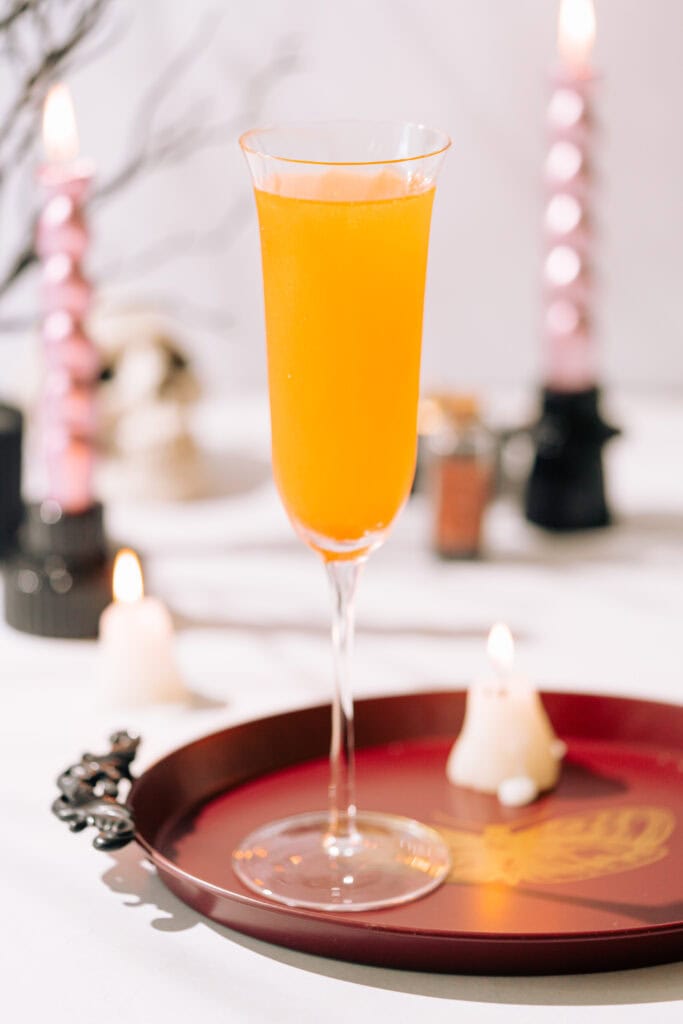 a champagne flute filled with an orange mimosa on a red tray