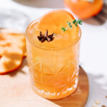 Spiced persimmon mocktail garnished with a persimmon slice, thyme and star anise.