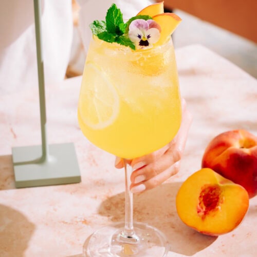 Holding the amalfi Spritz - Peach limoncello cocktail on a table with a lamp in the backfround