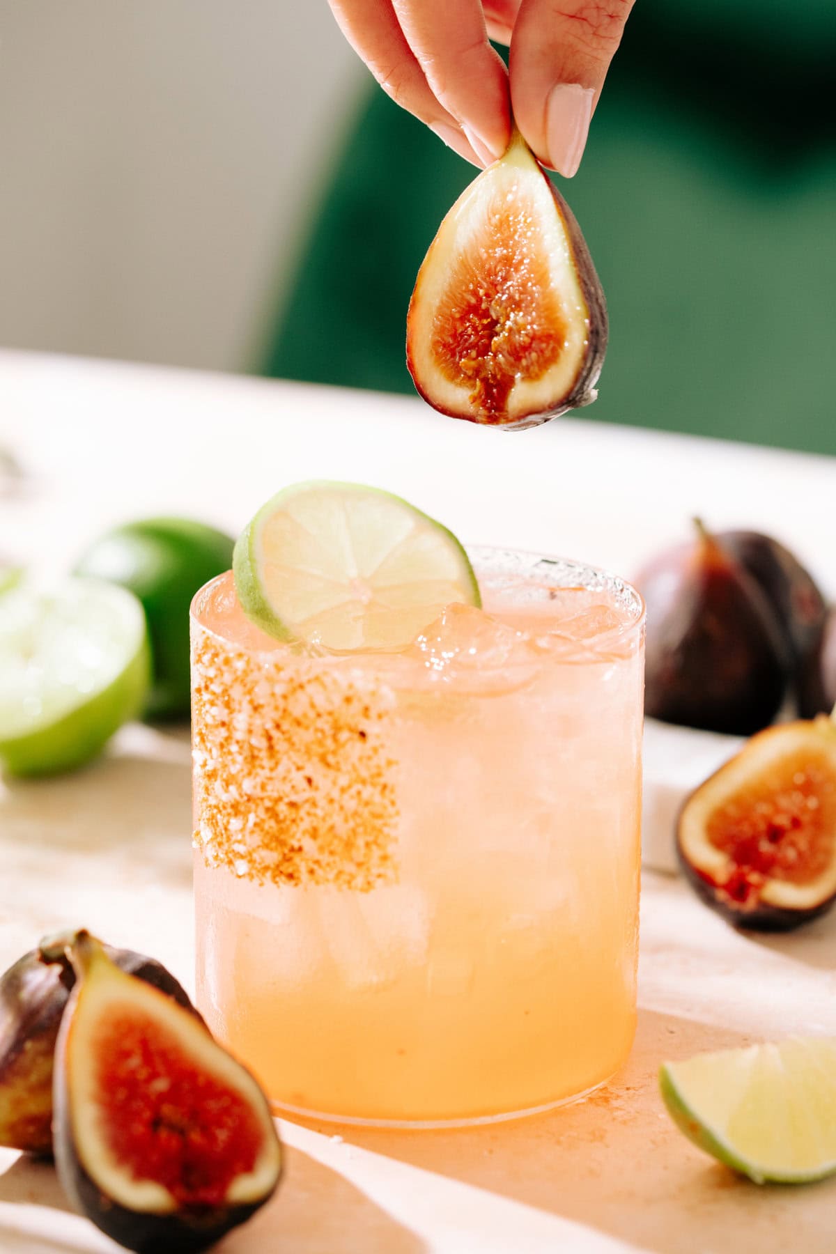 maple fig margarita cocktail with a fresh fig being placed in the glass. The rim is coated with sugar, salt, and cinnamon.