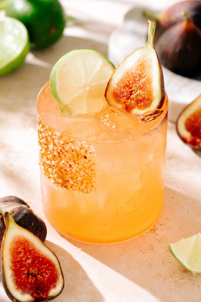 close up of maple fig margarita, with a slice of lime and half fig as a garnish. The rim is coated with a mixture of salt, sugar, and cinnamon.
