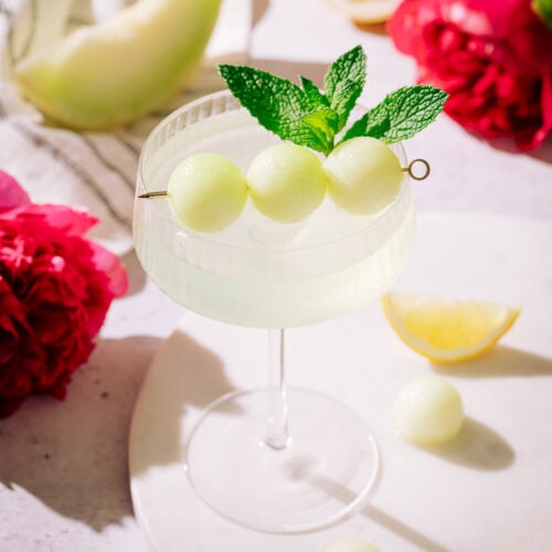 honeydew appletini cocktail on board, garnished with melon balls and mint