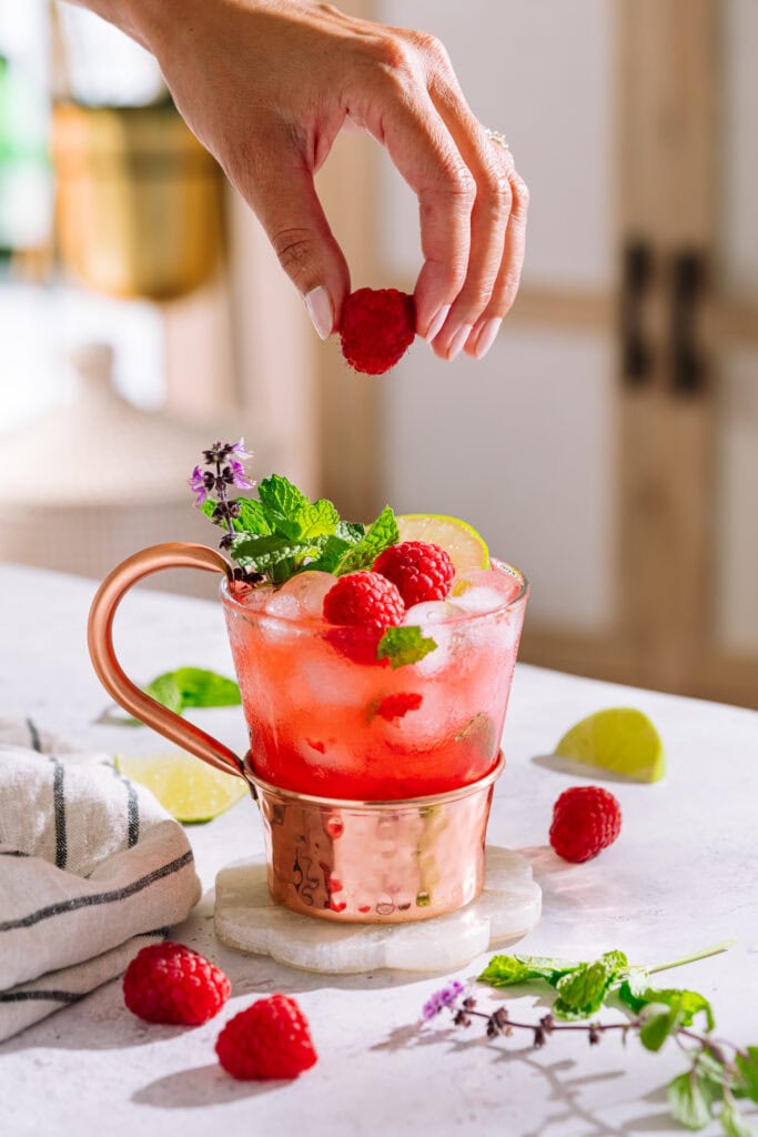 Raspberry moscow mule in glass and copper mug on coaster garnished with raspberries, lime and mint