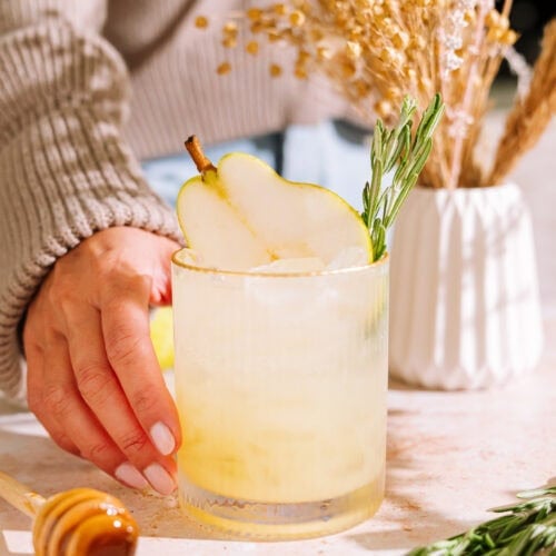 hand in tan sweater reaching for the rosemary pear mocktail.