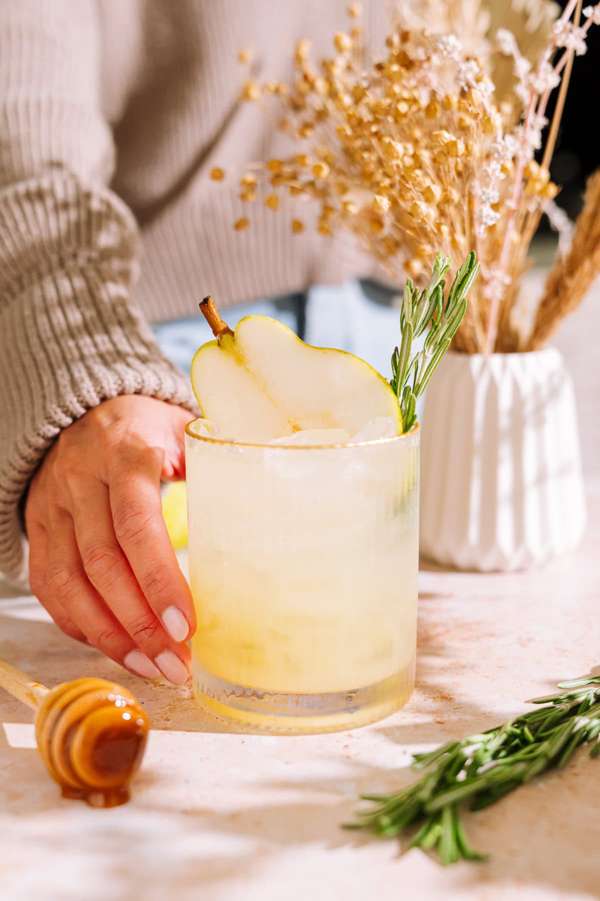 hand in tan sweater reaching for the rosemary pear mocktail.