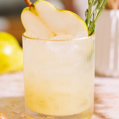 close up of rosemary pear mocktail on table with lemon in the background