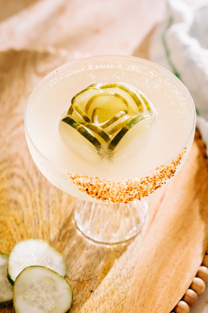 overhead shot of pickle cocktail with a pickle ice cube and tajin rim on table. A few slices of pickles are also on the table.