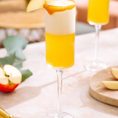 Bubbling Caramel apple mimosa with caramel rim, garnished with apple slice.