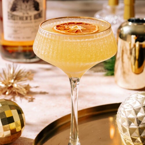 Glittering gold rush cocktail garnished with orange on gold tray