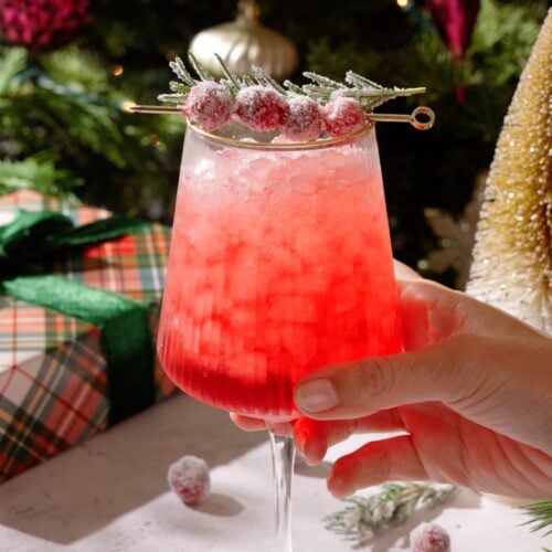 Cranberry Spritz Mocktail in front of Christmas tree garnished with sugared cranberries and rosemary