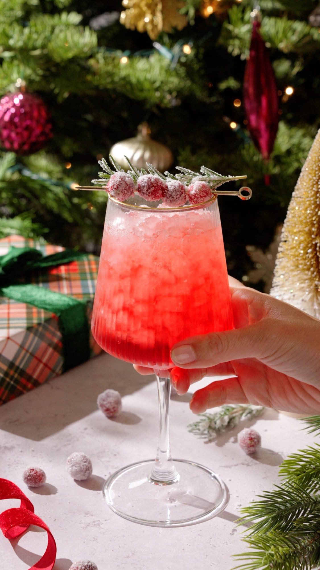 Cranberry Spritz Mocktail in front of Christmas tree garnished with sugared cranberries and rosemary