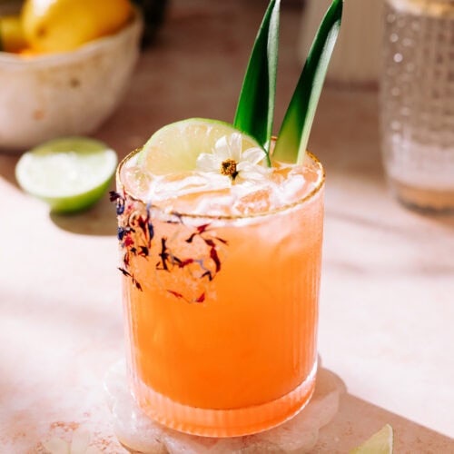 Tropical Aperol Margarita (with Coconut and Pineapple) in a short glass garnished with a slice of lime and edible flowers.