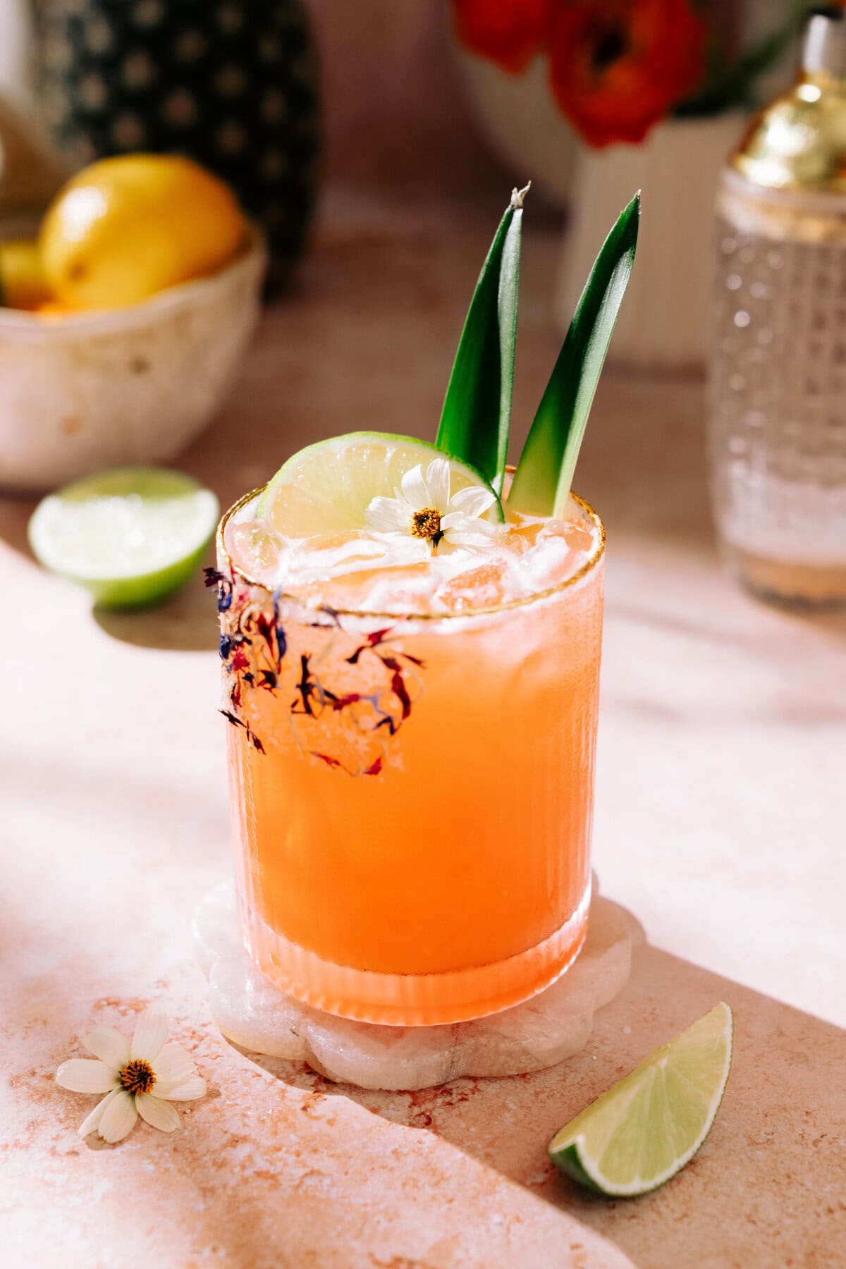 Tropical Aperol Margarita (with Coconut and Pineapple) in a short glass garnished with a slice of lime and edible flowers.