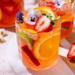 Summer fruit sangria with strawberries, citrus slices, and edible flowers.