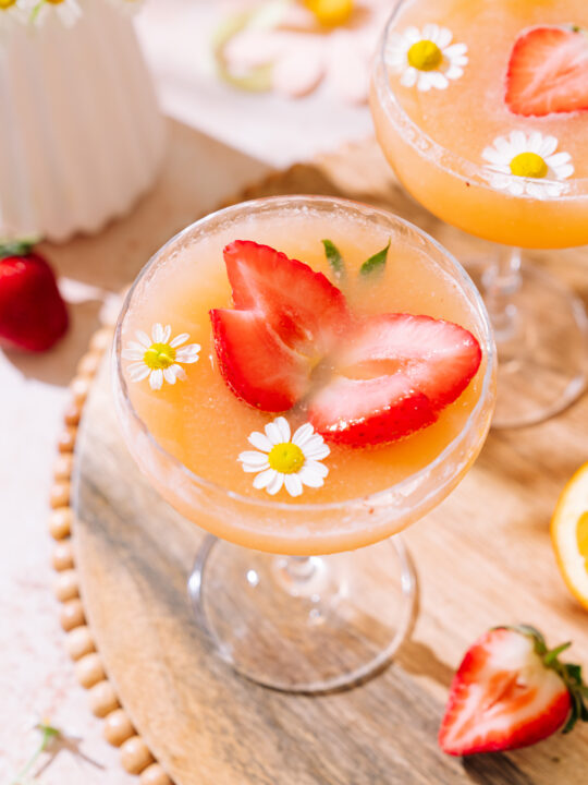 Strawberry mimosas recipe in 2 coupe glasses, garnished with strawberries and chamomile
