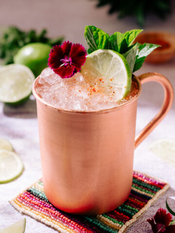 Tequila mule (mexican mule) in copper mug, garnished with lime, flower and mint