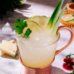 Pineapple Mezcal Mule cocktail with ice, pineapple, lime, and cilantro garnish in a copper-handled glass.