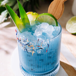 Blue hawaiian mocktail on tray, garnished with pineapple and lime