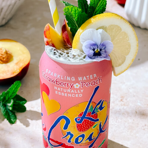 Peach Bellini Spritz mocktail in LaCroix can with lemon, peach slices, mint, and edible flower garnish."