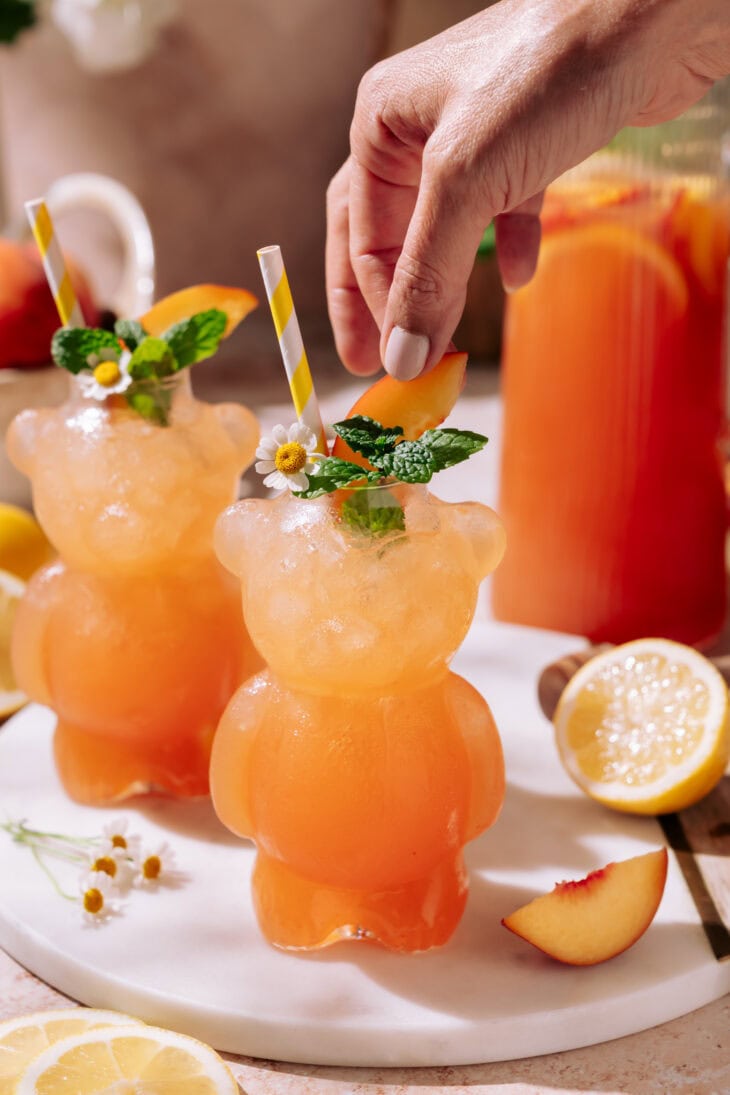 Hydrating Peach Lemonade served in two bear shaped glasses with ice, peach slices, lemon rounds, fresh mint, and chamomile flowers, with a refreshing summer vibe.