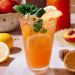 Hydrating Peach Lemonade served in a tall glass with ice, peach slices, lemon rounds, fresh mint, and chamomile flowers, with a refreshing summer vibe.