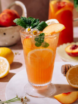 Hydrating Peach Lemonade served in a tall glass with ice, peach slices, lemon rounds, fresh mint, and chamomile flowers, with a refreshing summer vibe.