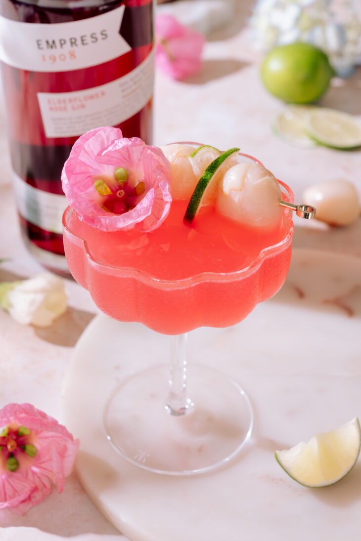 Sweet lychee martini with fresh lychee, lime, and pink flower garnish in a cocktail glass.