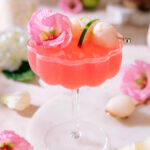 Sweet lychee martini with fresh lychee, lime, and pink flower garnish in a cocktail glass.