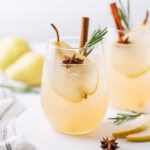 Spiced Pear Vodka Cocktail in a short glass garnished with a slice of a pear, anise, cinnamon stick and rosemary branch. In the background there is one more drink of the same description and 2 pears.