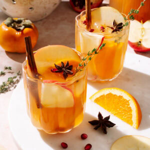 Two glasses of apple cider sangria garnished with apple slices, cinnamon sticks, star anise, and fresh thyme.