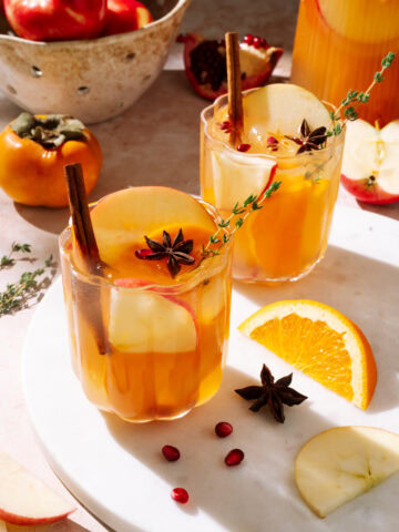 Two glasses of apple cider sangria garnished with apple slices, cinnamon sticks, star anise, and fresh thyme.