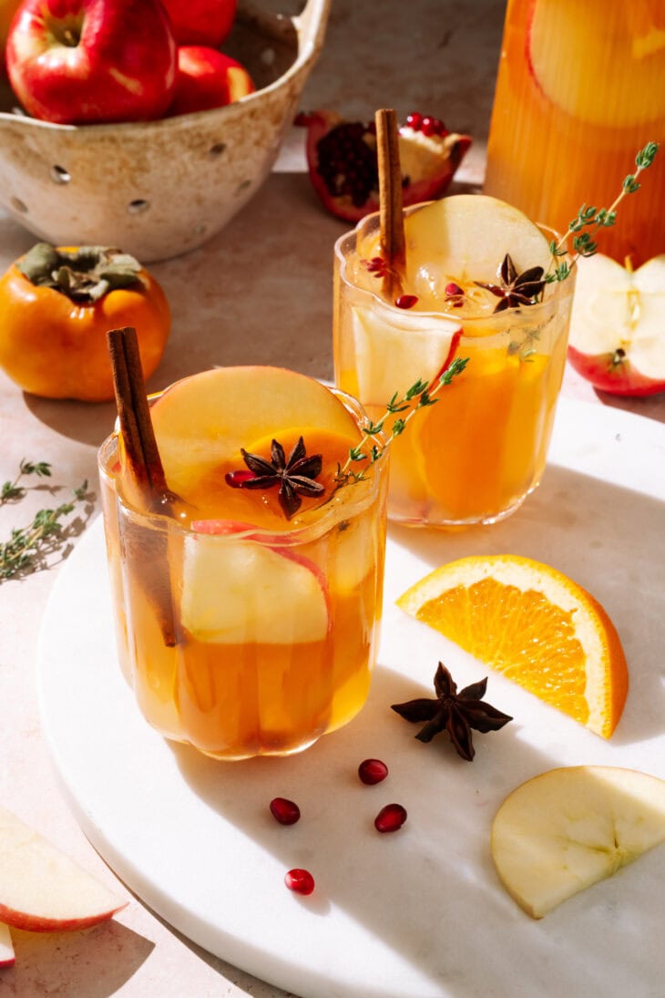 Two glasses of apple cider sangria garnished with apple slices, cinnamon sticks, star anise, and fresh thyme.