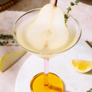 Pear martini garnished with a thin pear slice and fresh thyme in a cocktail glass.
