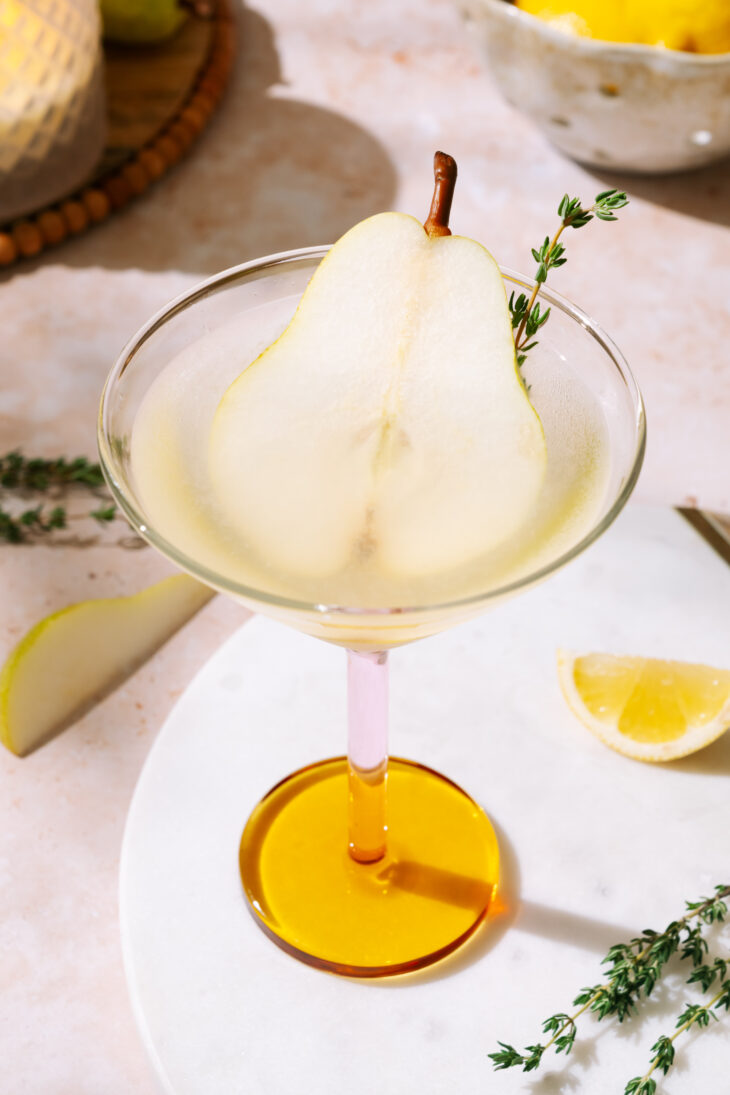 Pear martini garnished with a thin pear slice and fresh thyme in a cocktail glass.