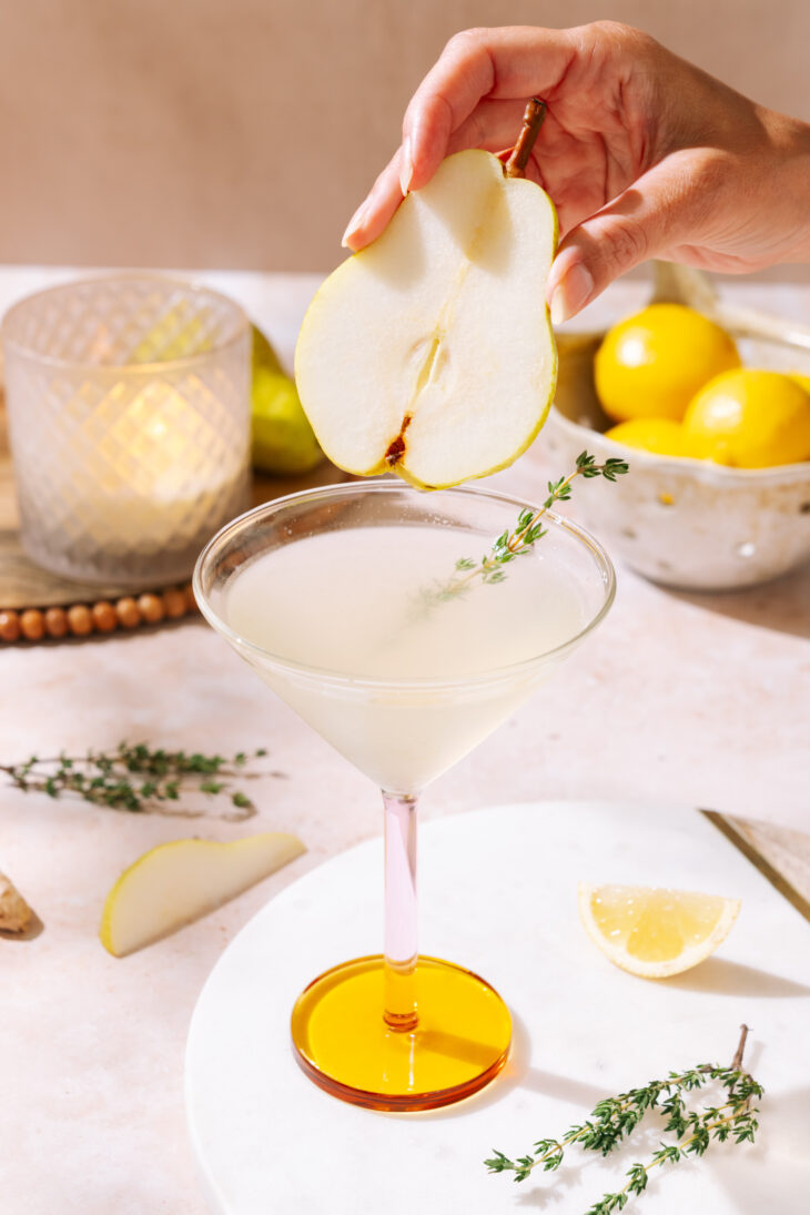 Pear martini garnished with a thin pear slice and fresh thyme in a cocktail glass.