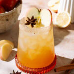 Spiced apple cider mocktail served over ice, garnished with apple slices and star anise, with a cinnamon-sugar rim.