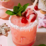 Close-up of the Cherry Merry Mocktail with a popsicle, mint garnish, and coconut-rimmed glass in a pink holiday setting.