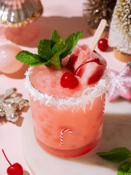 Close-up of the Cherry Merry Mocktail with a popsicle, mint garnish, and coconut-rimmed glass in a pink holiday setting.