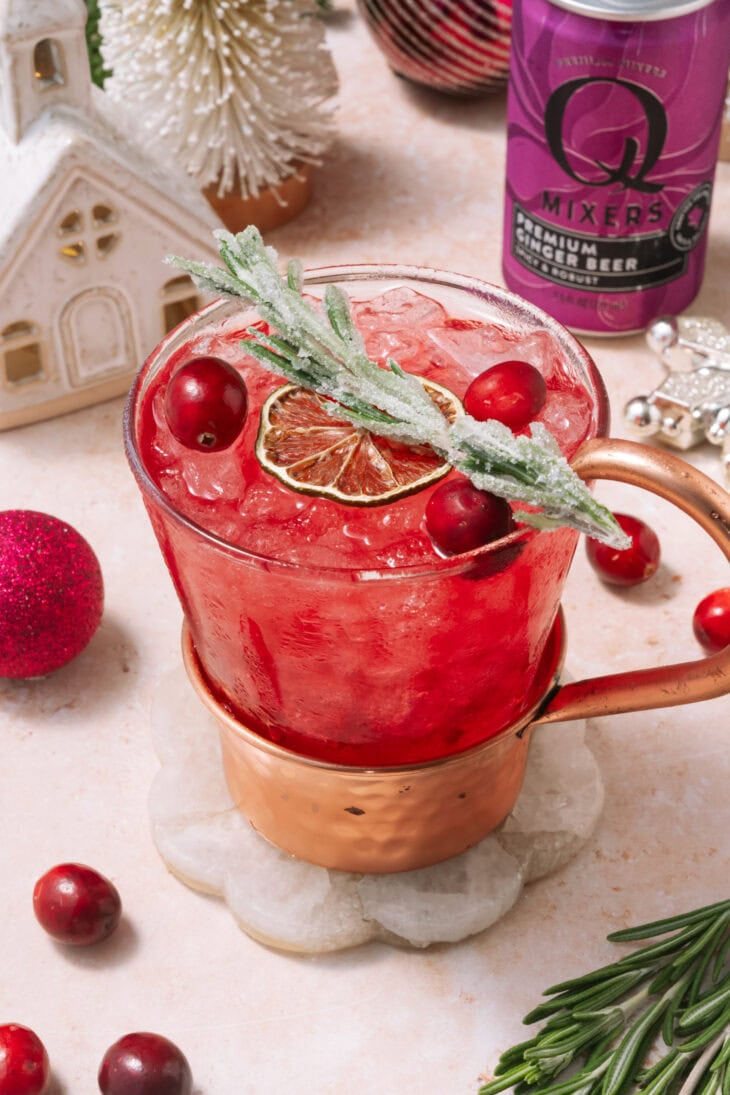 Cranberry Moscow Mule in a copper mug with ice, cranberries, sugared rosemary, and a dried citrus garnish.