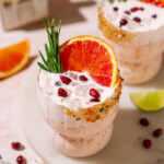 Festive Yuletide Limonada garnished with blood orange, rosemary, and pomegranate on a white marble surface.