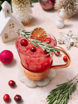 cranberry moscow mule in mug garnished with rosemary, cranberries and citrus