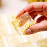 Hand holding a champagne jello shot with gold sugar sprinkles.
