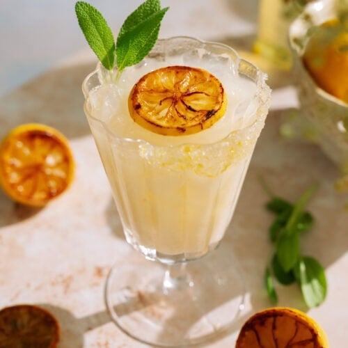 Creamy limoncello cocktail in a vintage glass, garnished with charred lemon and fresh sage.